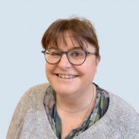 Photo of Jo wearing glasses and a grey jumper with a light blue background